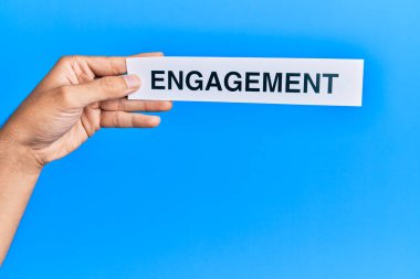 Kafkasyalı bir adam elinde kağıt tutarken mavi arka planda nişan sözcüğü var.