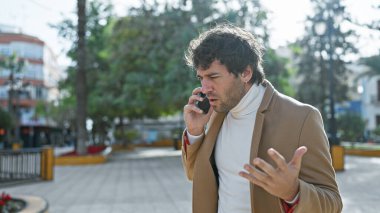 Şehir parkında telefonla konuşan İspanyol bir adam endişeli görünüyor.