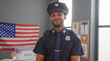 Gülümseyen Afro-Amerikan polis memuru bize karşı oy kullanma merkezinde bayrak sallıyor..