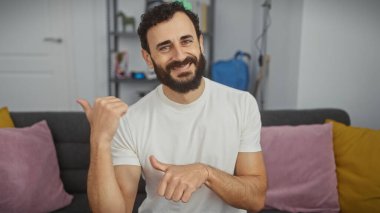 Sakallı adam oturma odasında parmaklarını yana doğru gösteriyor.