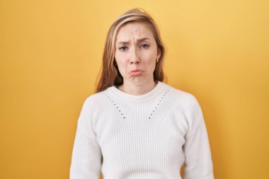 Sarı arka plan üzerine beyaz kazak giyen genç beyaz bir kadın depresyonda ve sıkıntıdan endişeli, sinirli ve korkmuş bir şekilde ağlıyor. hüzünlü ifade. 