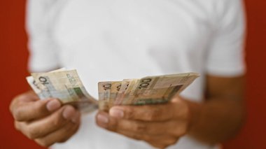 Genç bir İspanyol adam, kırmızı duvara karşı izole edilmiş, Polonya zloti parası sayıyor..