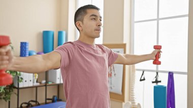 Dambıllarla egzersiz yapan genç bir İspanyol adam. Parlak bir fizik tedavi kliniğinde.