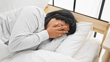 Sıkıntılı, orta yaşlı bir kadın. Eli alnında uzanmış, parlak bir yatak odası düzeninde..