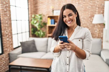 Genç, güzel, İspanyol bir kadın evde akıllı telefon kullanıyor.