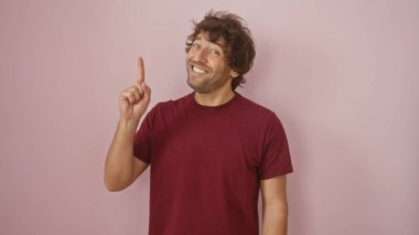 Kıvırcık saçlı ve sakallı neşeli genç bir adam pembe bir duvara yaslanmış iyimserliği ve günlük tarzını temsil ediyor..