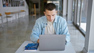 Üniversite kütüphanesinde dizüstü bilgisayarla çalışan İspanyol bir adam, konsantrasyon ve kararlılığı yansıtıyor..