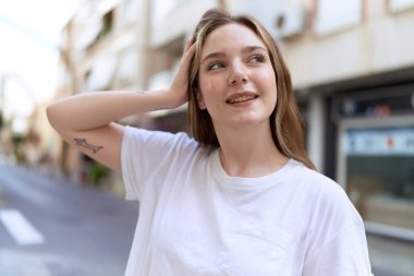 Beyaz kadın gülümsüyor. Kendinden emin. Caddenin kenarına bakıyor.