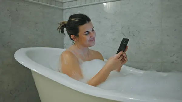Smiling Young Woman Enjoys Bubbly Bath While Using Her Smartphone — Stock Photo, Image