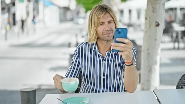 在城市的室外咖啡馆里 一个留着长发的英俊男人用智能手机 桌上放着咖啡 — 图库照片