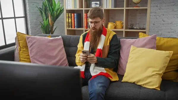 Brodatego Młodzieńca Używającego Smartfona Leżącego Kanapie Domu Otoczonego Kolorowymi Poduszkami — Zdjęcie stockowe