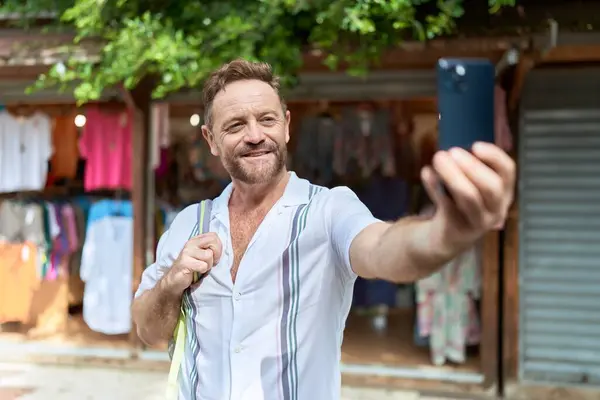 Middle age man tourist smiling confident making selfie by the smartphone at street market