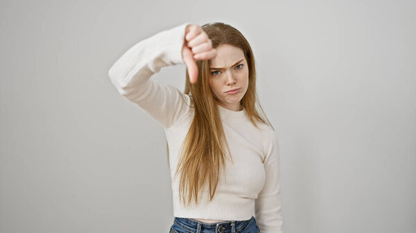 A disappointed young woman giving a thumbs down gesture against a white background expresses disapproval.