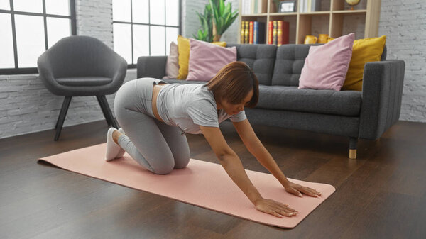 Молодая женщина растягивается на розовом коврике для йоги в современной гостиной, воплощая оздоровление и активный образ жизни.