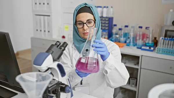 焦点を当てた女性科学者が科学機器と顕微鏡に囲まれた実験室でフラスコを調べる — ストック写真