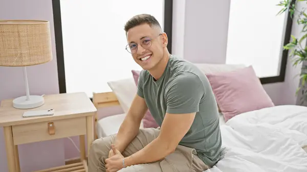 Young Hispanic Man Smiling While Sitting Comfortably Modern Bedroom Setting — Stock Photo, Image
