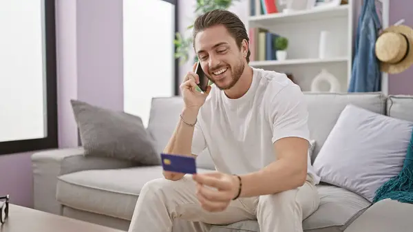 Young Hispanic Man Talking Smartphone Holding Credit Card Sitting Sofa — Stockfoto