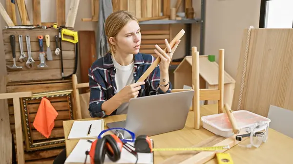 Fokuseret Blond Kvinde Undersøger Træstykker Tømrerværksted Omgivet Værktøjer Bærbar Computer - Stock-foto