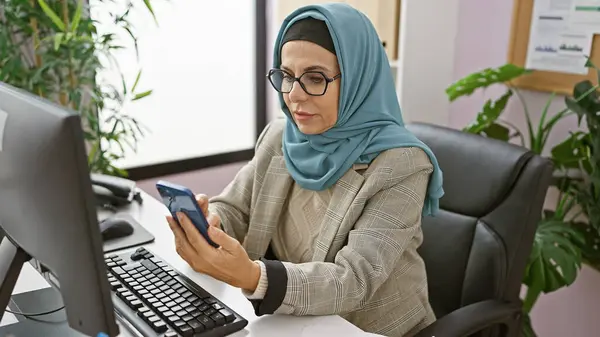 Eine Professionelle Frau Hidschab Mit Smartphone Ihrem Modernen Schreibtisch Inmitten lizenzfreie Stockbilder