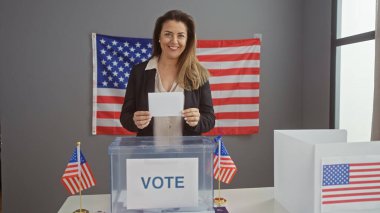 Gülümseyen kadın Amerikan bayraklarıyla ABD oy kullanma merkezinde oy kullanıyor.