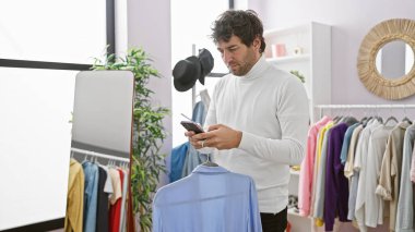 Modern bir gardıropta şık bir adam akıllı telefonunu çeşitli asılı kıyafetlerin arasında karıştırıyor..