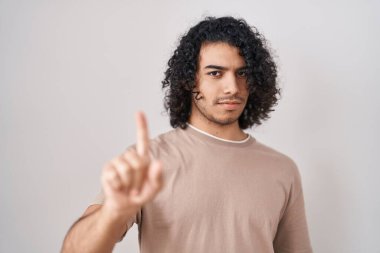 Beyaz arka planda duran kıvırcık saçlı İspanyol adam parmağını kaldırmış ve kızgın bir ifadeyle işaret ediyor. 