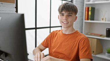 Sarışın, beyaz bir çocuk kütüphane masasında oturmuş akademik çalışmalar için bilgisayar kullanıyor..