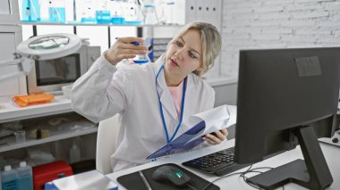 Odaklanmış bir kadın bilim adamı laboratuvar ortamında mavi bir sıvıyı test tüpünde inceliyor..