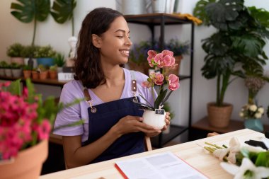 Young african american woman florist smiling confident holding plant at flower shop