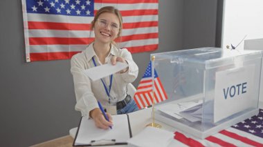 Gülümseyen genç bir kadın arka planda Amerikan bayrağıyla ABD seçimlerinde oy kullanıyor.