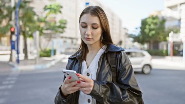 Kafkasyalı esmer kadın güneşli şehir caddesinde akıllı telefon kullanıyor.
