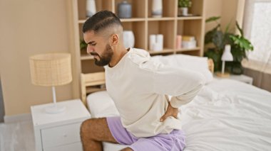 Güzel döşenmiş bir yatak odasında yatarken sırt ağrısı çeken yakışıklı bir adam..