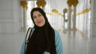 Süslü bir camide parlayan güneş ışığıyla parlayan başörtüsü takmış gülümseyen genç bir kadın..