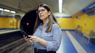 Madrid metro istasyonunda akıllı telefon kullanan güzel İspanyol bir kadın metroda bekliyor.