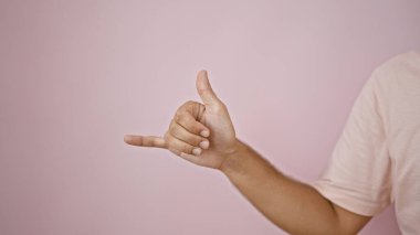 Young hispanic man makes a surfer hand gesture against a pink wall, isolated and expressive. clipart