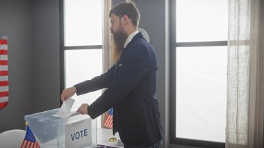 Amerikan bayraklarıyla dolu bir odadaki oy sandığında oy kullanan sakallı bir adam..
