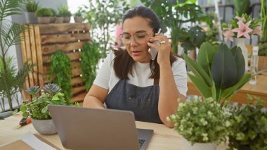 Önlüklü olgun bir kadın çiçekçi, çiçekçi dükkanında dizüstü bilgisayarla konuşuyor..