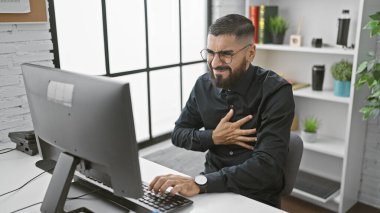 Modern işyerinde göğüs ağrısı çeken yakışıklı sakallı bir adam.