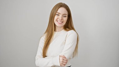 Beyaz kazaklı, kolları çapraz beyaz arka planda gülümseyen güzel, beyaz bir kadın.