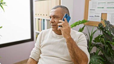 Modern ofis ortamında akıllı telefon kullanan olgun İspanyol bir adam profesyonel ama sıradan bir iş ortamı yaratıyor..