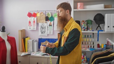 Kizil sakalli adam renkli bir terzi dükkaninda boyut bandi kullaniyor moda eskizleri ve kumaslari olan.