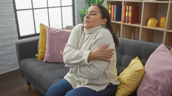 Middle Aged Hispanic Woman Embraces Herself While Sitting Couch Cozy — Stock Photo, Image