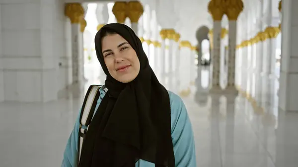 一位戴着头巾 面带微笑的年轻女子站在一座华丽的清真寺里 明亮的阳光反射在光滑的地板上 — 图库照片