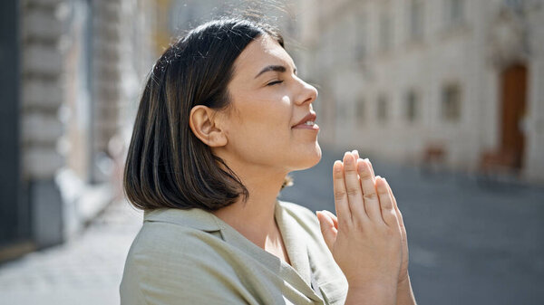 Young beautiful hispanic woman praying with closed eyes at cafeteria