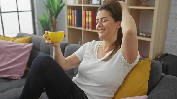 stock image Relaxed hispanic woman enjoying coffee in cozy living room, exuding casual elegance and comfort.