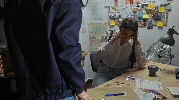 stock image A woman investigator overwhelmed in a cluttered board-filled police office, with a male colleague standing.