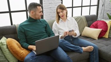 Bir adam ve bir kadın, modern bir oturma odasında teknolojinin tadını çıkarıyorlar..
