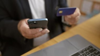 Üst düzey yöneticilerin elleri, ofis masasındaki akıllı telefondan alınan kredi kartıyla online alışverişe girişiyor.