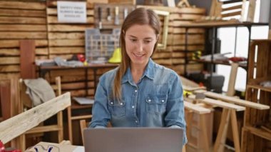 Kırsal marangozluk atölyesinde dizüstü bilgisayar üzerinde çalışan genç bir girişimci. Etrafı aletler ve ahşaplarla çevrili..