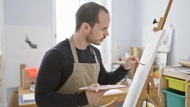 Sakallı bir adam, parlak bir sanat stüdyosundaki tuvale resim yapıyor..